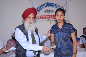 Dr. Gurmeet Singh, MD, President of Astha Vikas Samiti in Rajasthan, an NGO supported by IFCARE is handing over a chcke to Kum. Anjali Sain, a student in the local school. 